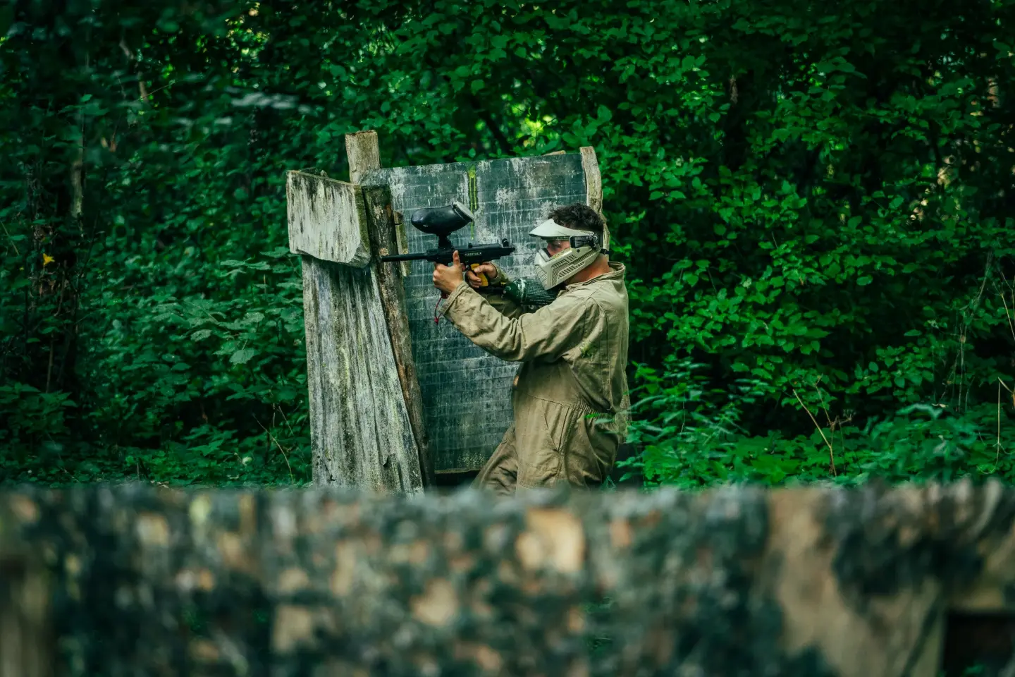 Paintballspeler mikt vanachter een houten bunker op het speelveld