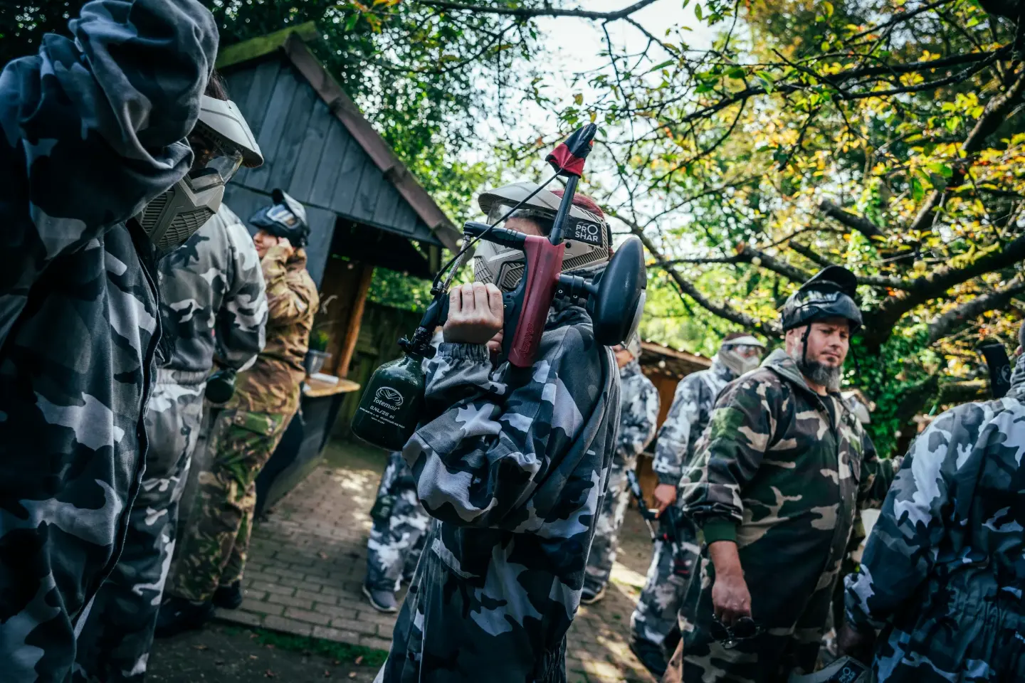 Paintballspeler in grijze camouflage-overall met zijn marker over de schouder in de safetyzone
