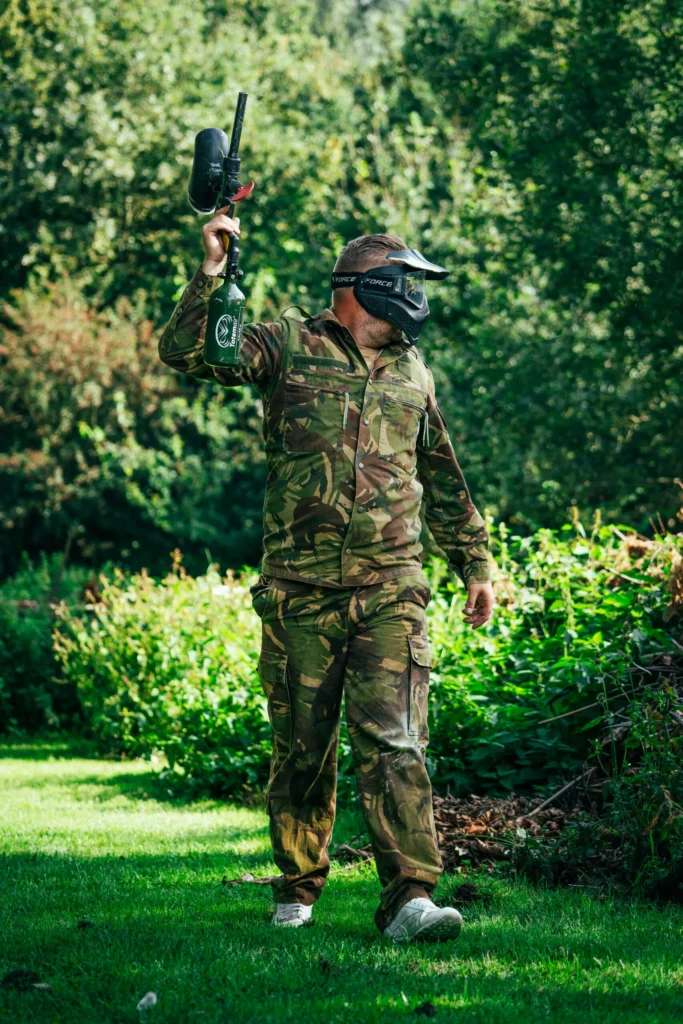 Paintballspeler in camouflagepak houdt zijn paintballmarker omhoog nadat hij geraakt is