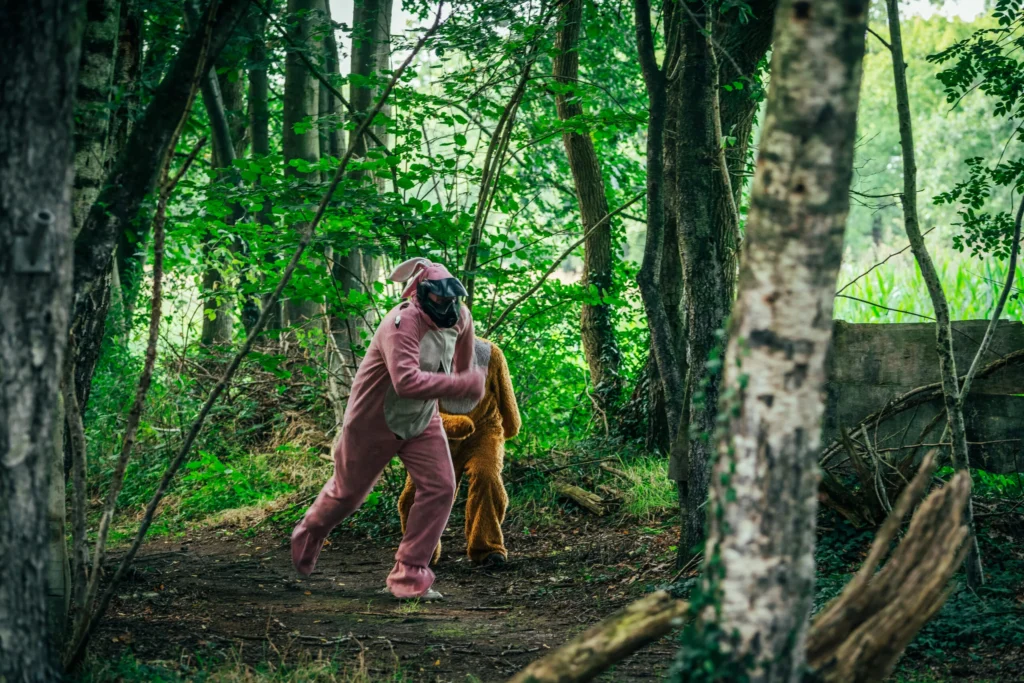 Vrijgezel in roze konijnenpak met paintballmasker sluipt met een speler in berenpak door het bos