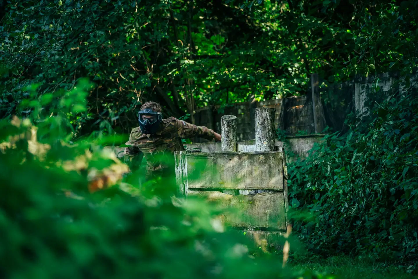 Paintballspeler zoekt dekking achter een houten obstakel tussen het groen